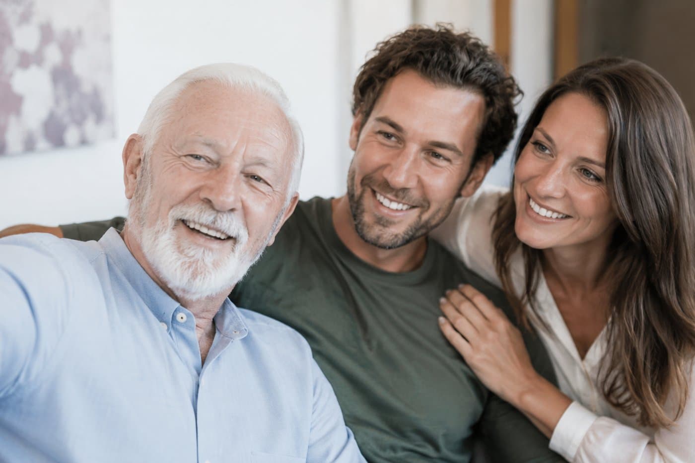 Een lachende oudere man maakt een selfie met zijn volwassen zoon en dochter thuis op de bank